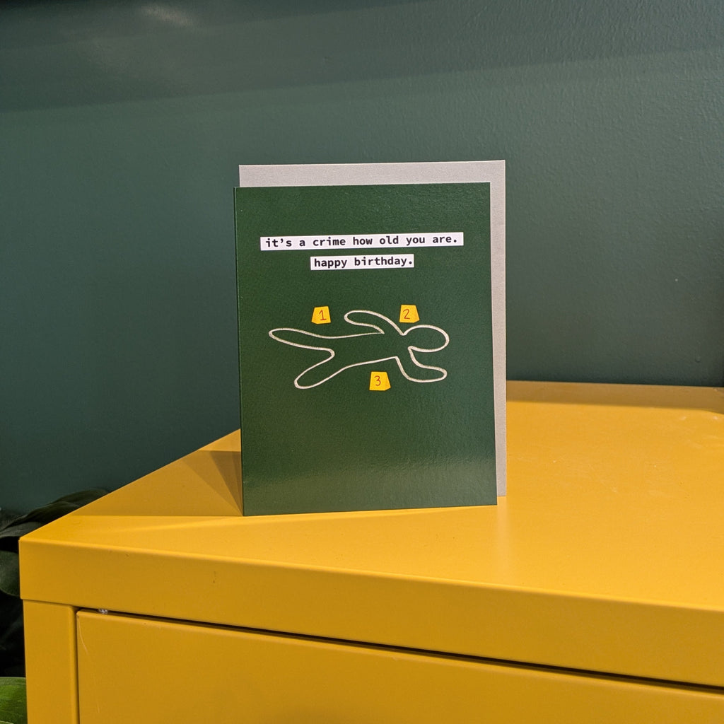 Green birthday card on a yellow surface with a green wall and shelf in the background