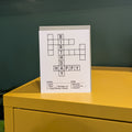 Happy Birthday crossword puzzle card on a yellow surface with a green wall in the background