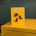 Yellow card with an  illustrated cowboy hat and boots on a yellow surface against a green wall.