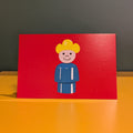 Card with a cartoon character on a red background, placed on a yellow surface.