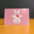 Pink card with a white rabbit illustration on a wooden surface
