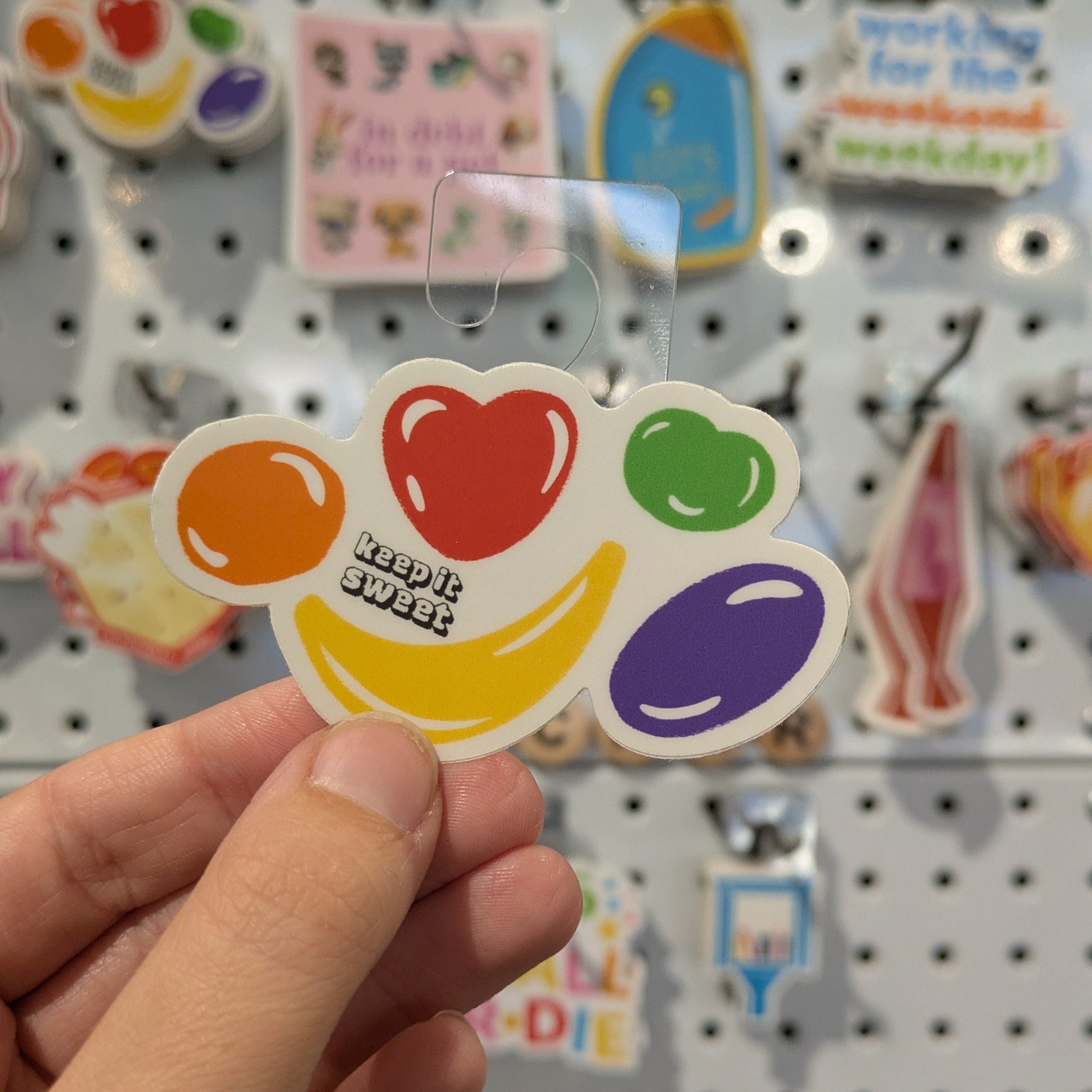 Colorful fruit candy sticker held by a hand with a pegboard background
