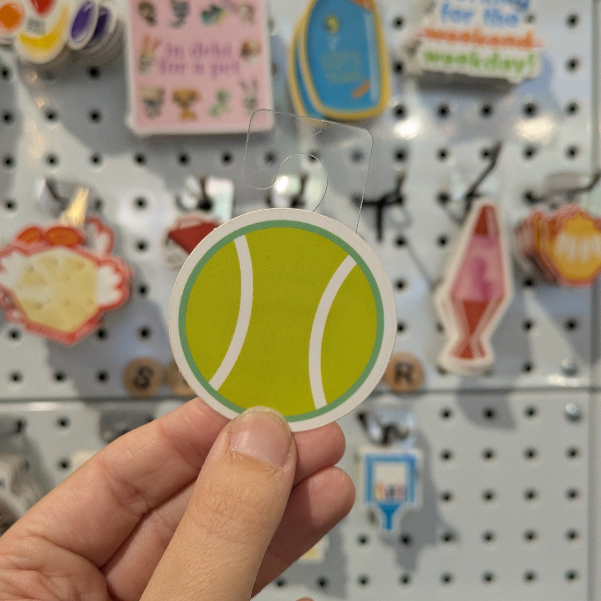 Hand holding a round green sticker with a white circle, against a pegboard background with various other stickers.