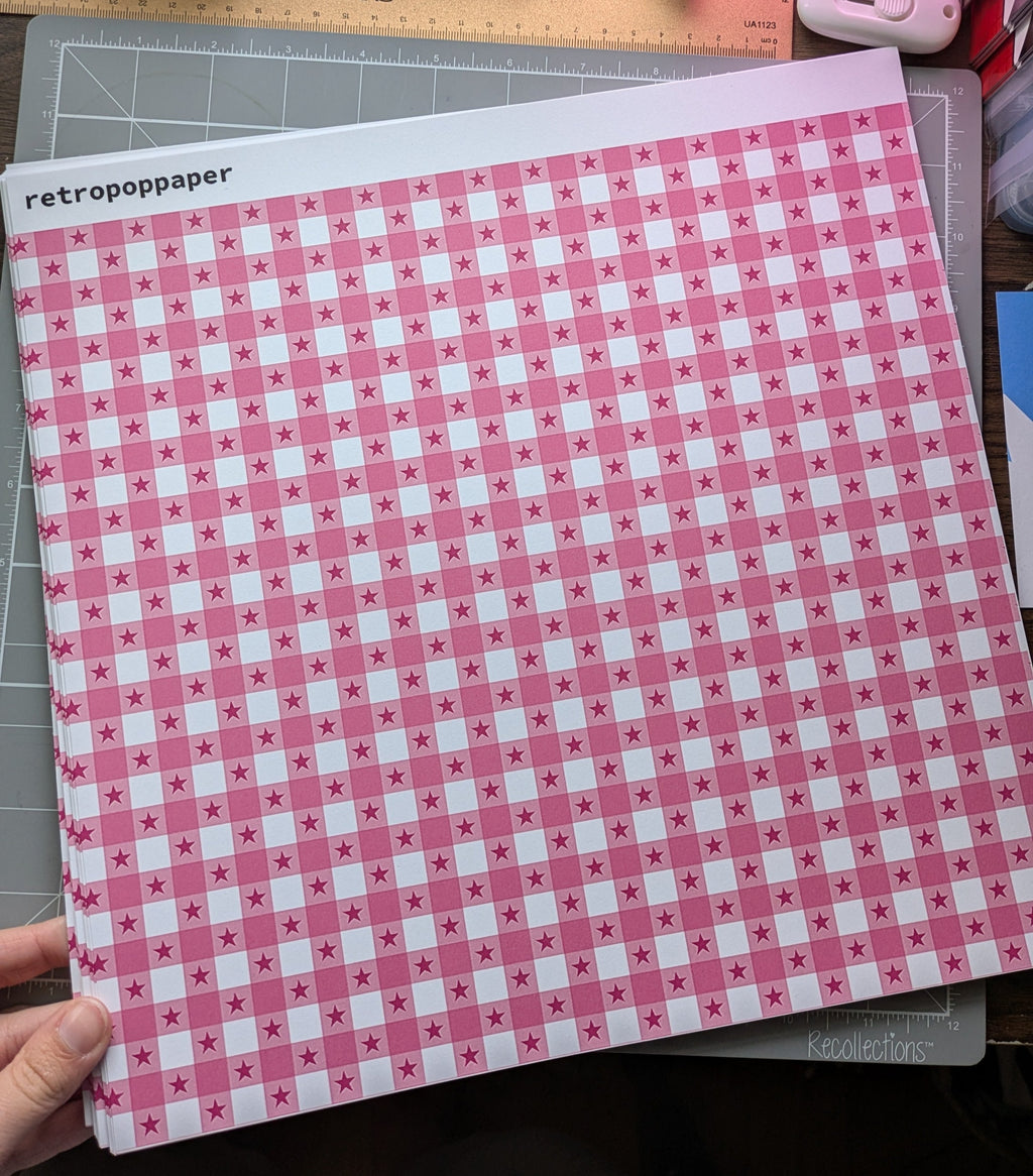 Pink and white checkered paper held by a hand with stationery items in the background.