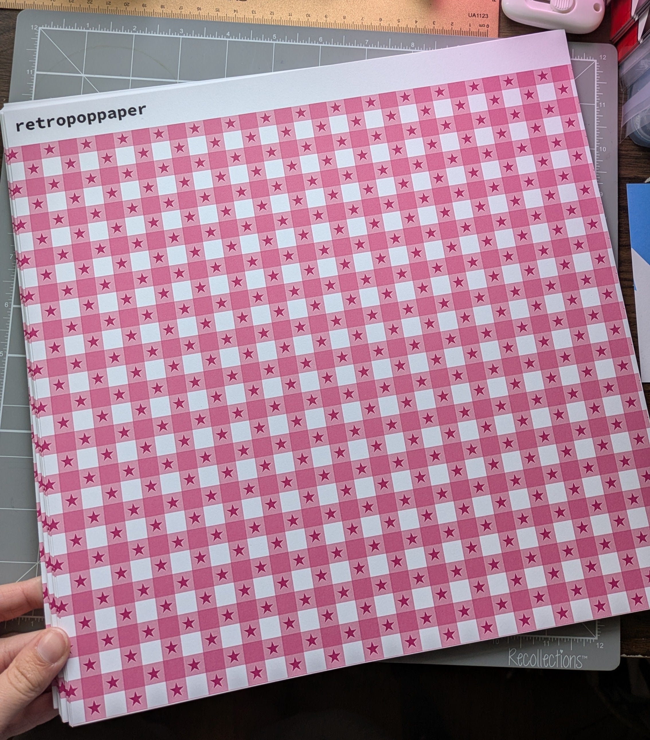 Pink and white checkered paper held by a hand with stationery items in the background.