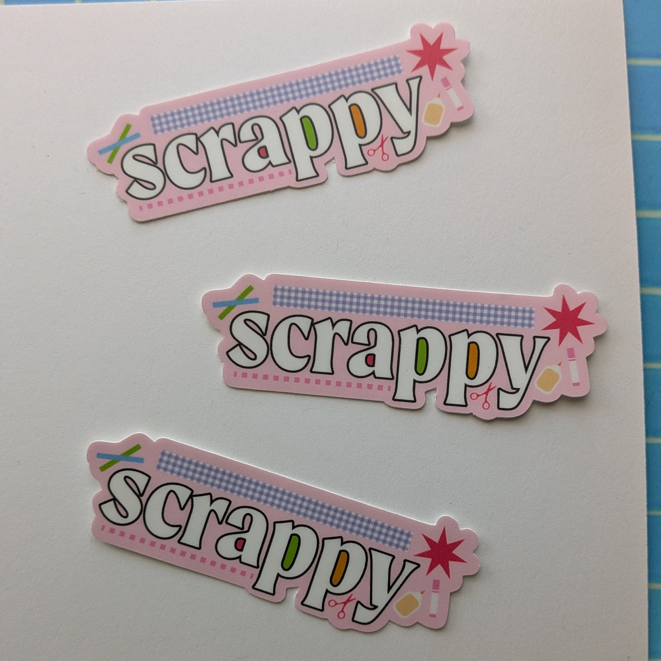 Three decorative paper strips with 'scrap' text on a blue grid background