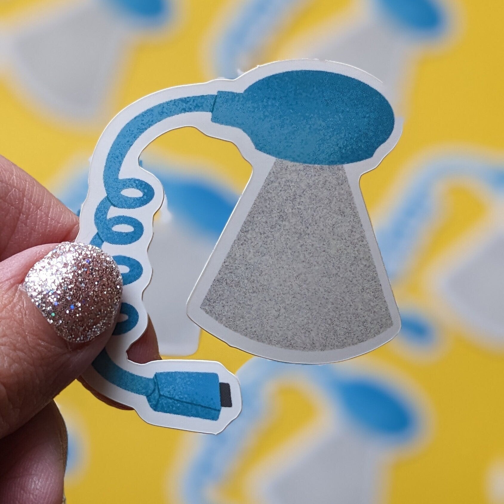 Hand holding a sticker of a blue worm light against a yellow background with blue shapes.